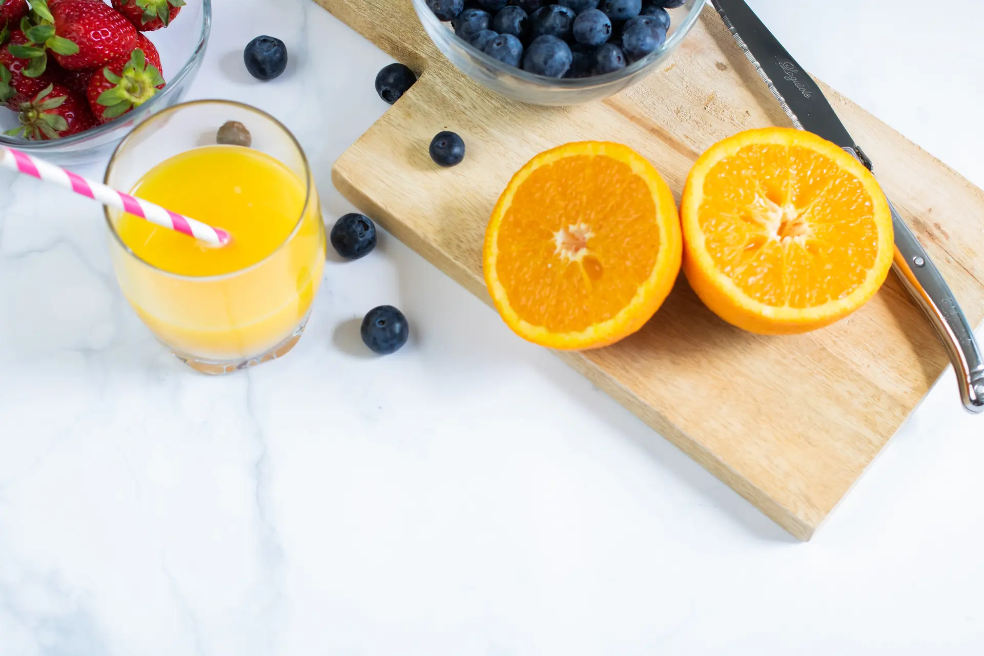 Un verre d’orange pressée, deux moitiés d’orange sur la planche, des myrtilles