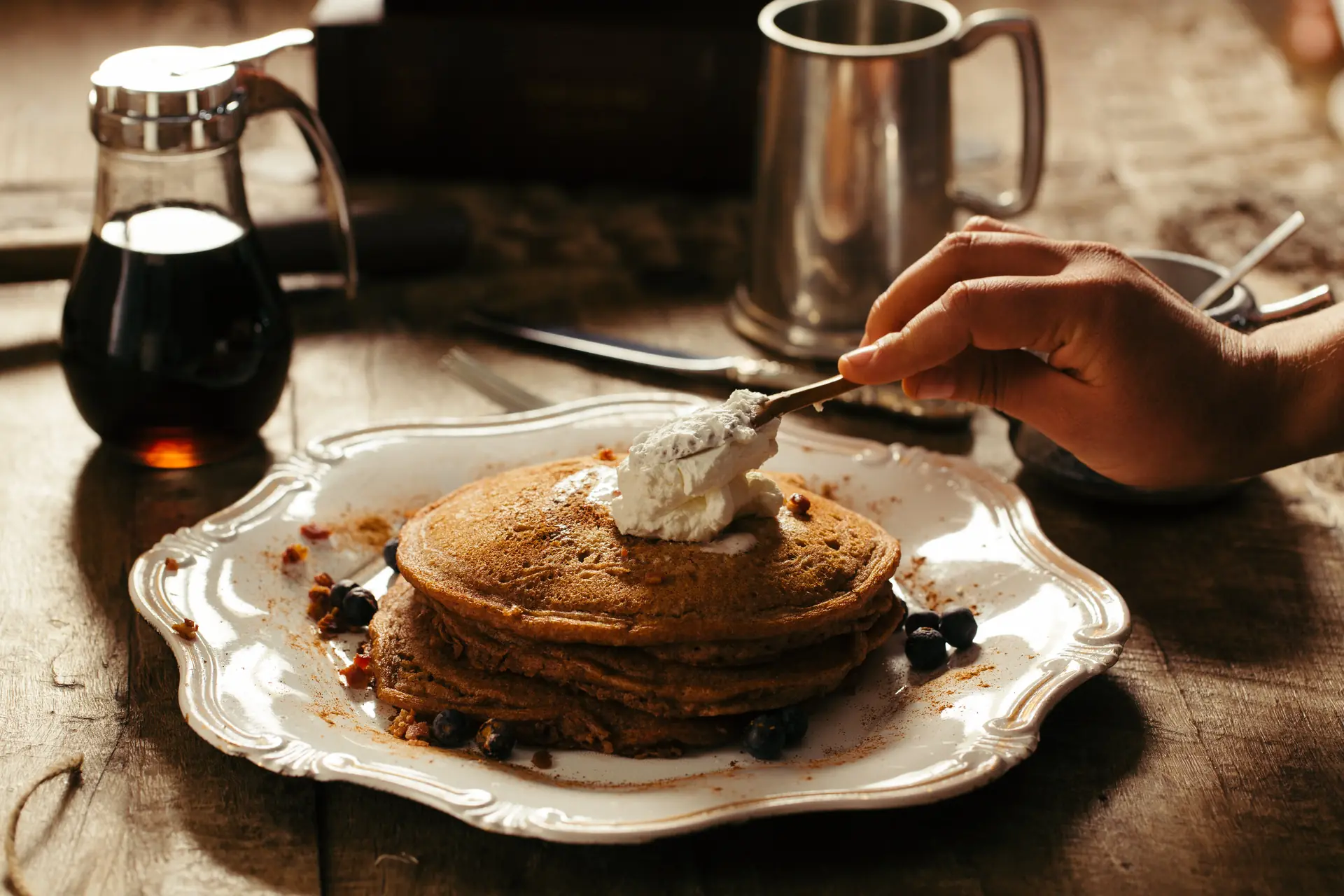 On pose la chantilly sur les pancakes au sarrasin et aux myrtilles, le sirop à côté